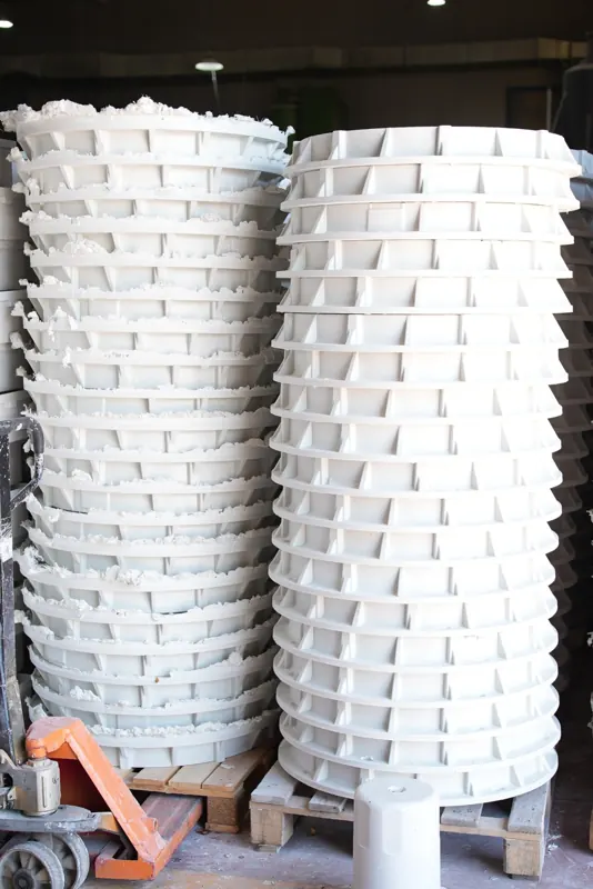 Tall stacks of circular composite manhole risers inside the production hall.