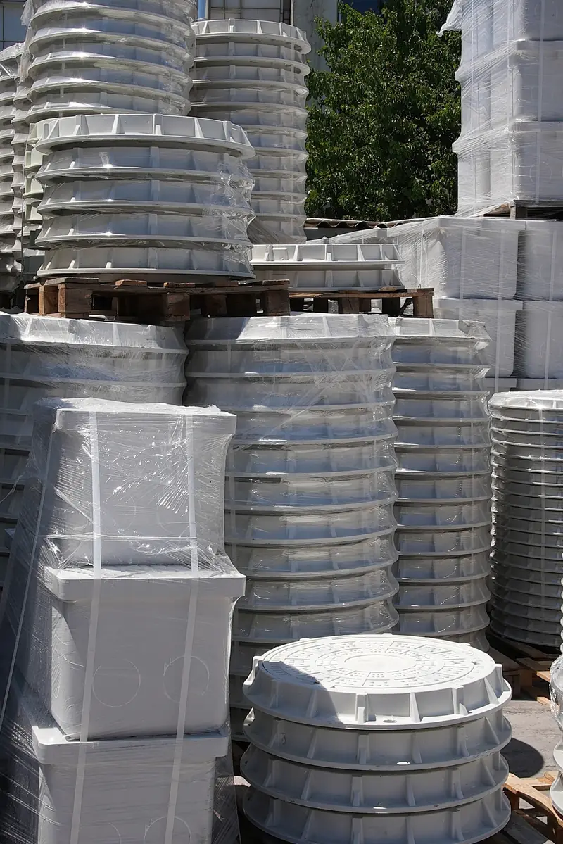 Circular composite manhole cover risers on pallets in the yard.
